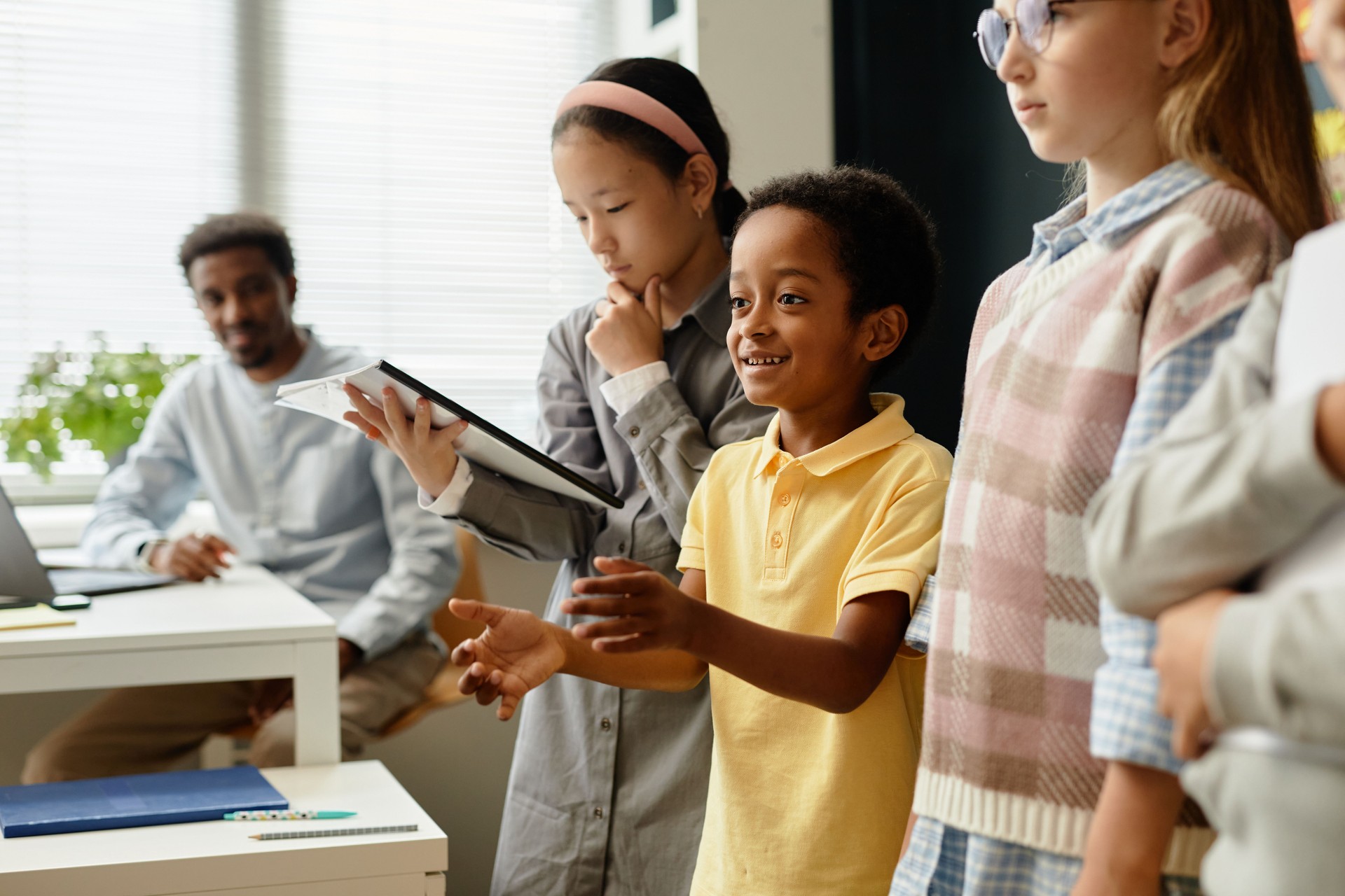 Male Student Speaking in Front of Class Standing in Line with Children during Lesson